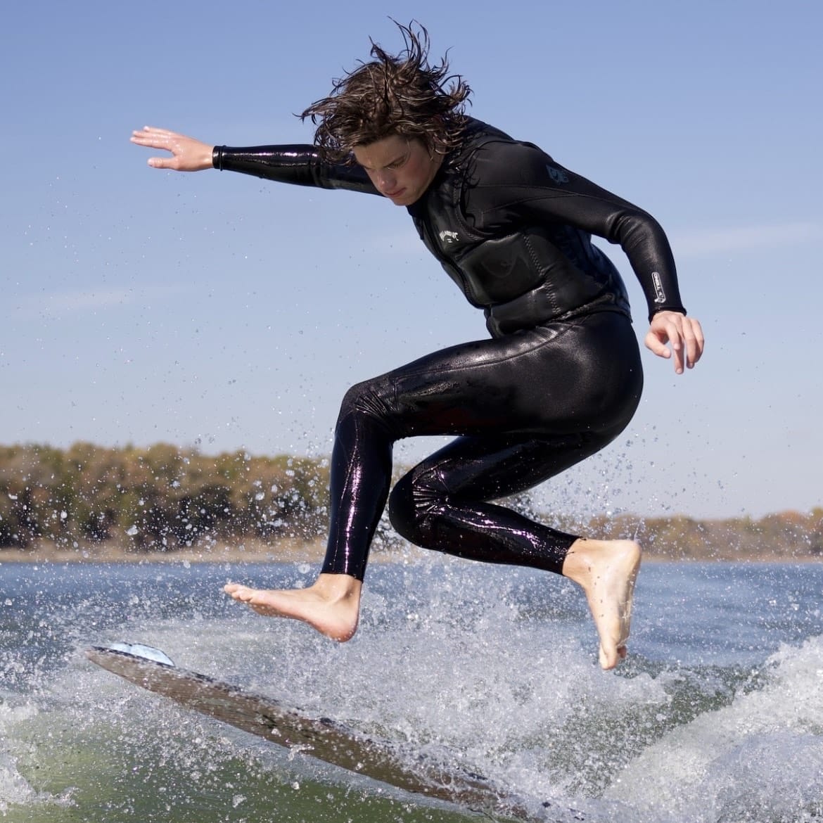 A man in a black wetsuit riding a surfboard.
