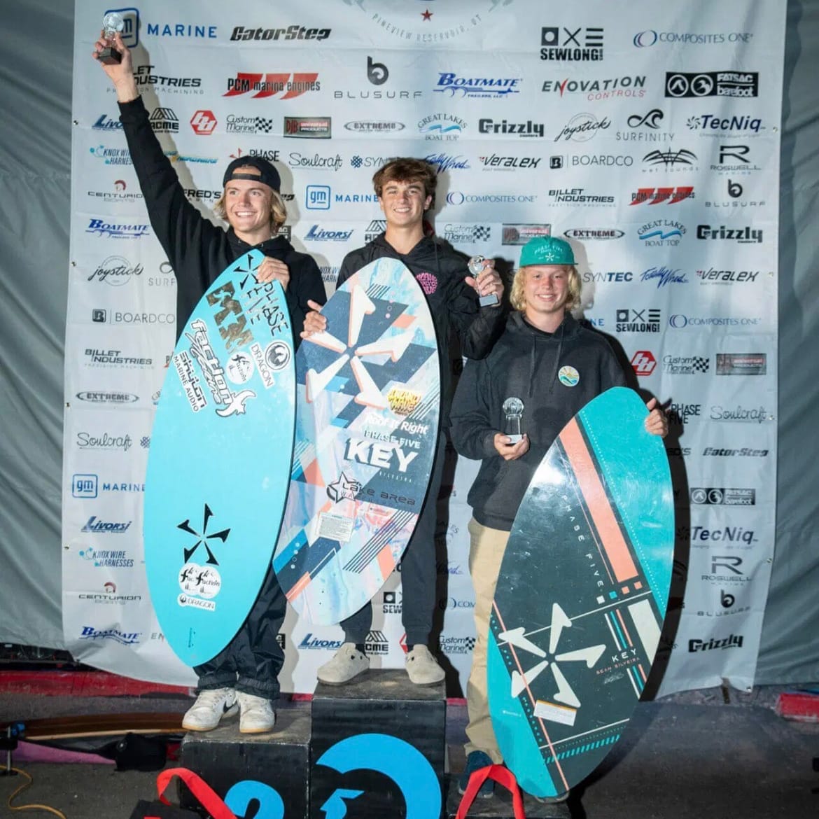 Cade Lybeck and two other surfers standing on top of a podium with their boards.