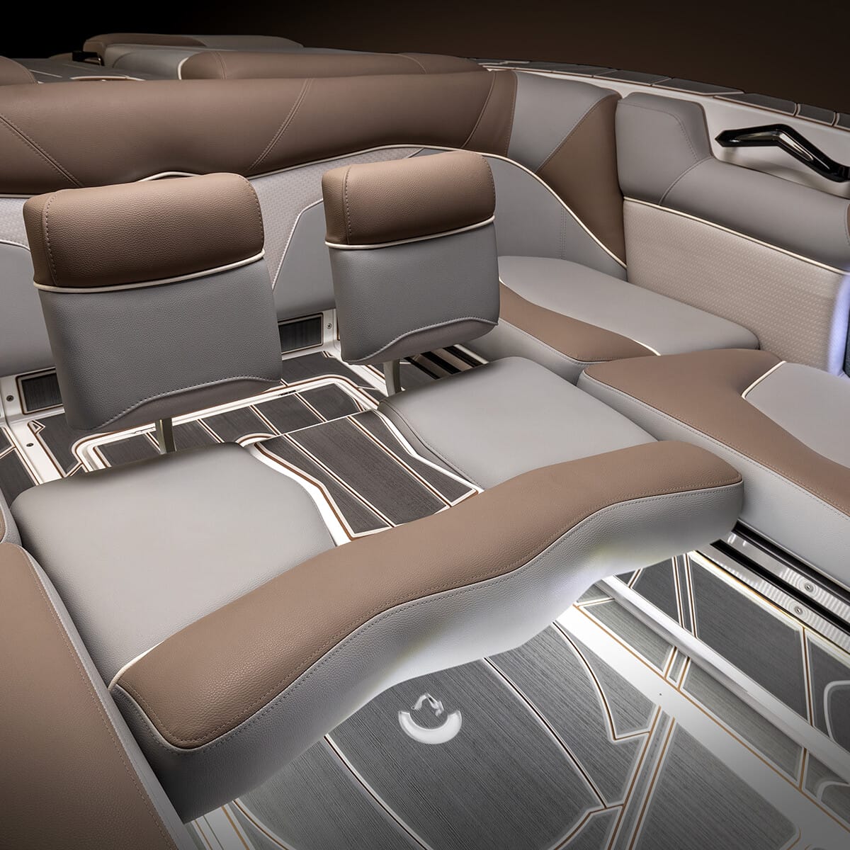 Interior of a modern boat with cushioned seats and armrests, featuring a brown and gray color scheme, built-in speakers, and potentially convertible seating for lounging.