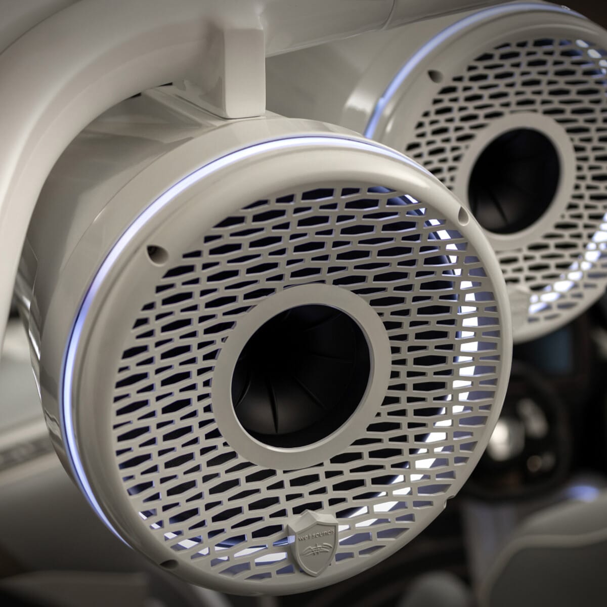 Close-up view of two mounted white speakers with circular grilles and illuminated edges, installed in a vehicle interior.