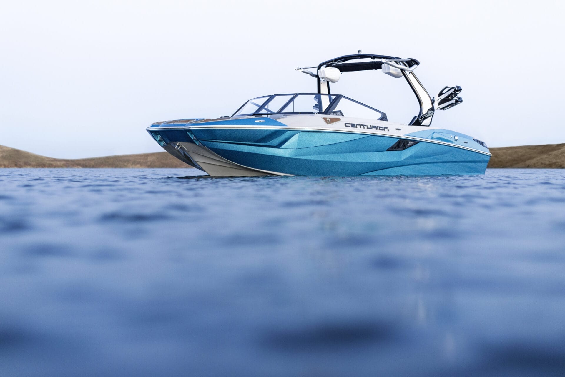 A blue and white Centurion speedboat is on the water, photographed from a low angle with distant land visible in the background.