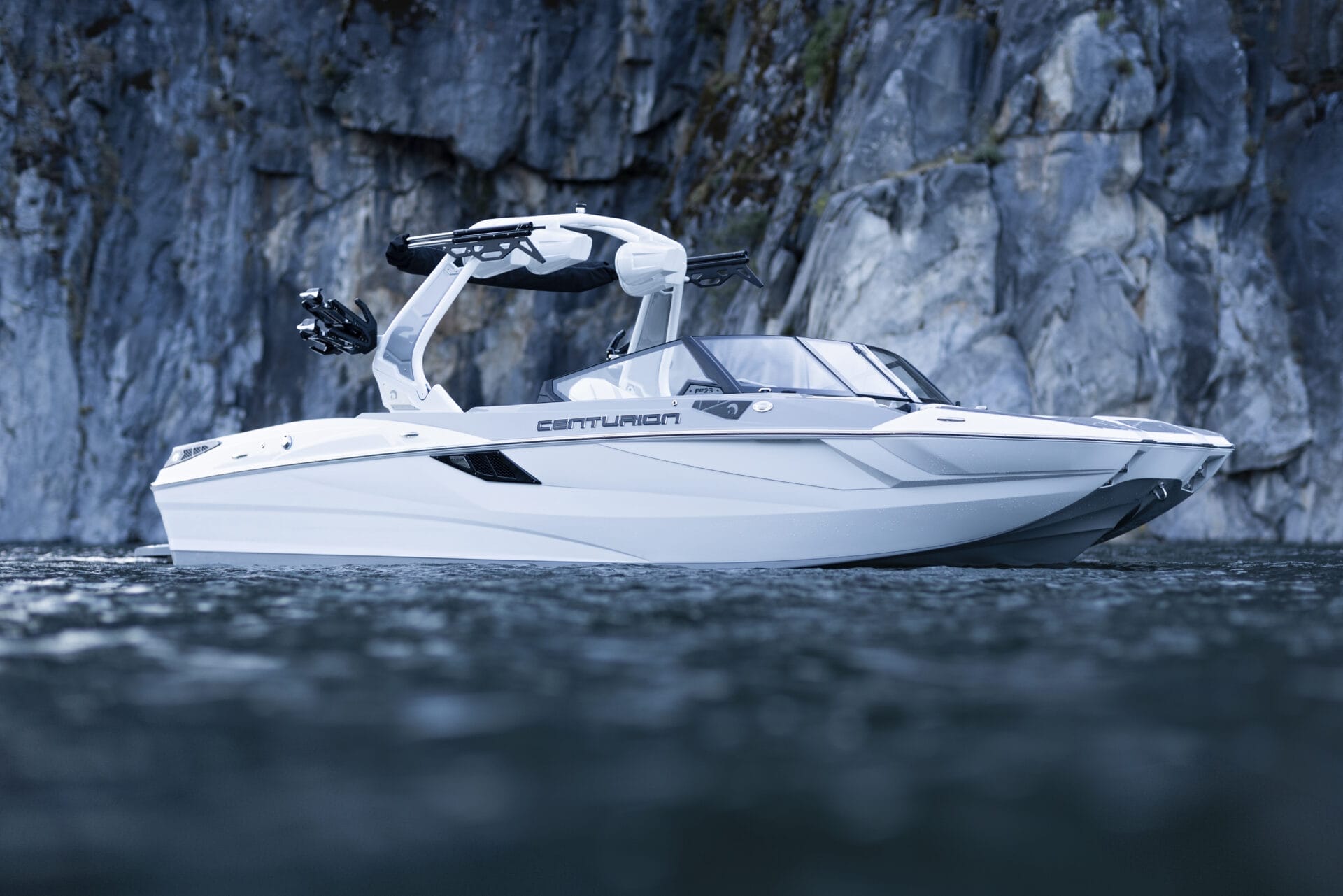 A white Centurion boat floating on water with a rocky cliff in the background.