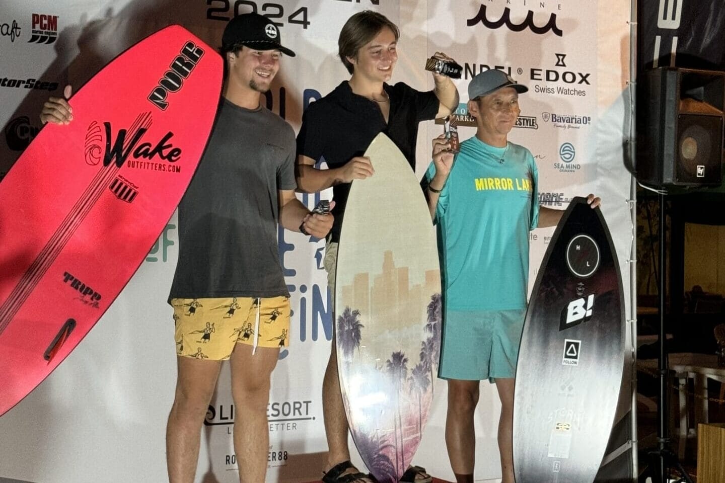Three people stand on a winners' podium at the Centurion Wake Surf Japan Open 2024, each holding surfboards and trophies. The backdrop features event and sponsor logos.