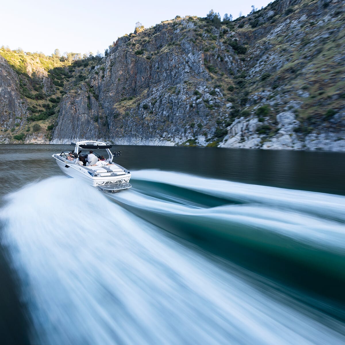 A speedboat rapidly moves through a narrow river with steep, rocky cliffs on either side, creating a wake behind it.