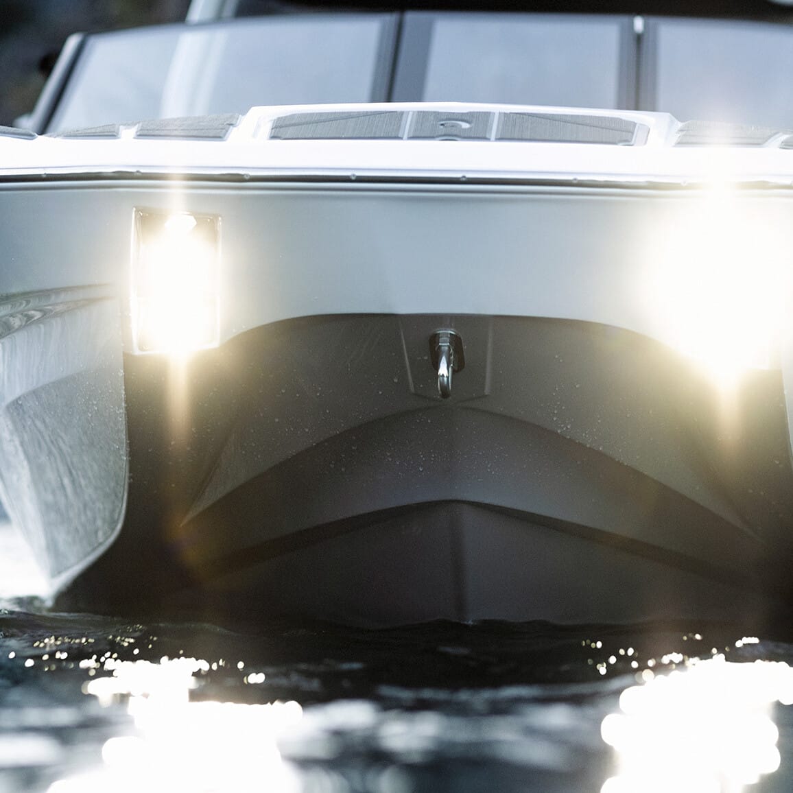 A close-up of the front of a boat with its headlights on, floating on a body of water.