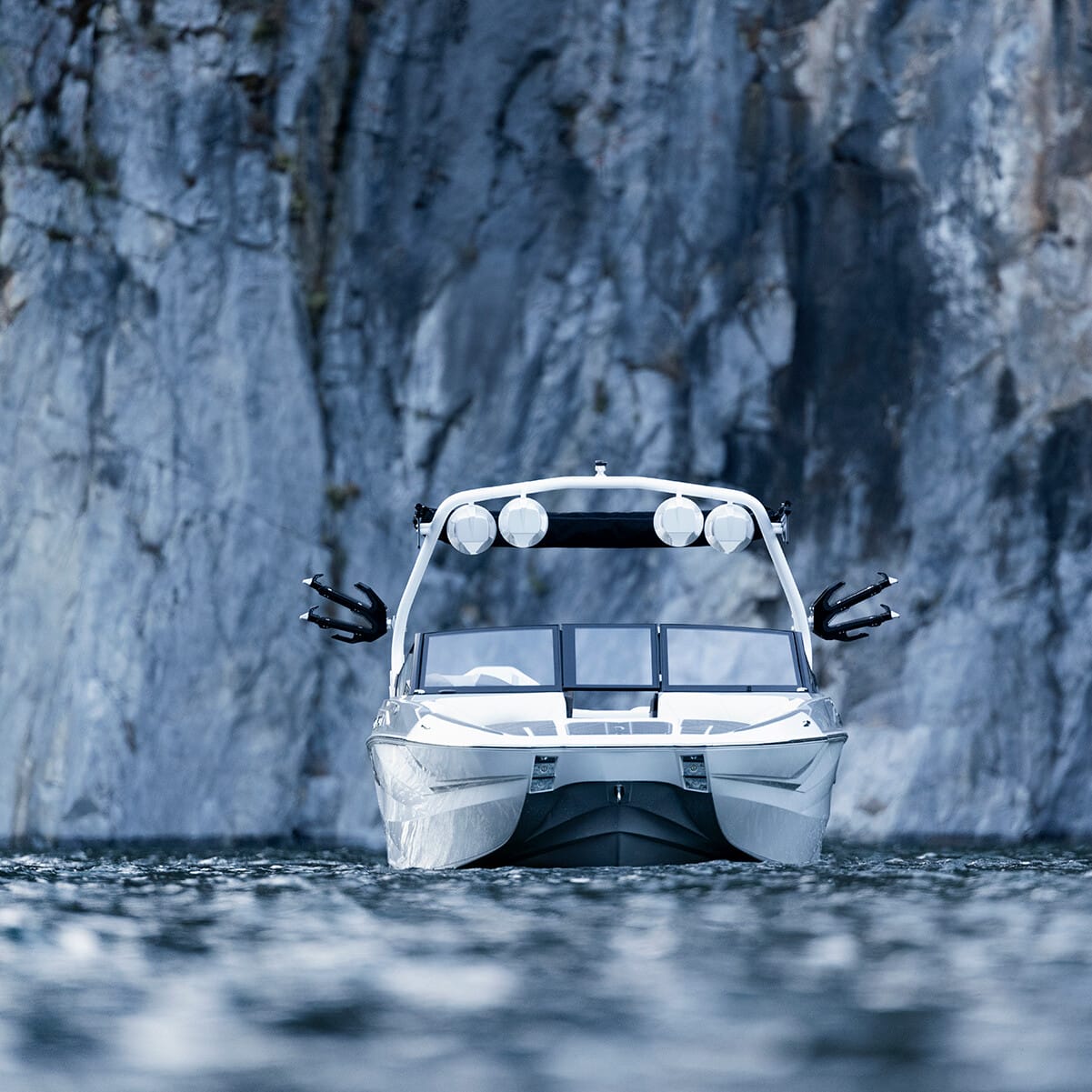 A white boat on the water, heading towards a rocky cliff face.